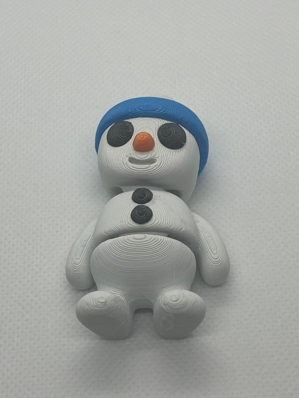 Small snowman figurine with a blue hat on a light gray background